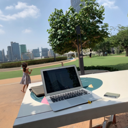 Laptop on a table and a child playing in a park at the background